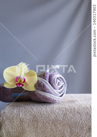 Rolled lilac towel with orchid on beige towel against gray background with copy space. Rolled lilac towel with orchid on beige towel against gray background with copy space. 140317903