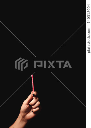 Hand holding a pink striped candle against dark background Hand holding a pink striped candle against dark background 140318004