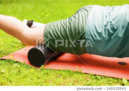 Close-up of a leg foam rolling on a mat over grass for myofascial release, self-massage, and post-workout recovery to relieve muscle tension. Close-up of a leg foam rolling on a mat over grass for myofascial release, self-massage, and post-workout recovery to relieve muscle tension. 140318543
