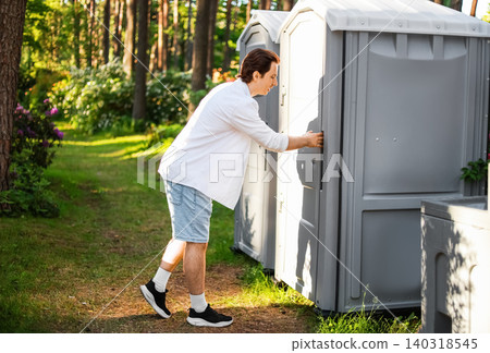 Man urgently opening an outdoor portable toilet door, dealing with an emergency like gastrointestinal problems, an upset stomach, or sudden diarrhea. Man urgently opening an outdoor portable toilet door, dealing with an emergency like gastrointestinal problems, an upset stomach, or sudden diarrhea. 140318545