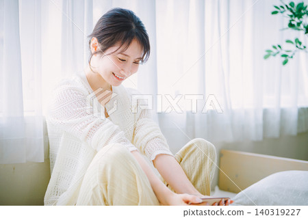 年輕女子坐在床上,看著她的智能手機 年輕女子坐在床上,看著她的智能手機 140319227