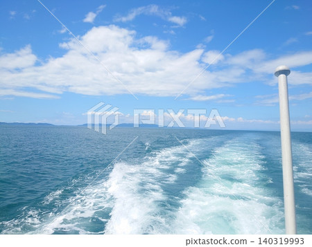 A view of the ocean wake and blue sky from the stern of a moving ship. 140319993