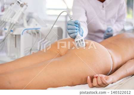 Cosmetologist using cold hammer for hardware procedure on buttocks of woman Cosmetologist using cold hammer for hardware procedure on buttocks of woman 140322012