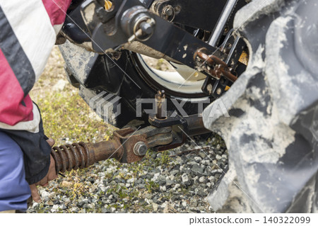 A farmer's hands handling the connecting pins and joints of a tractor implement. 140322099