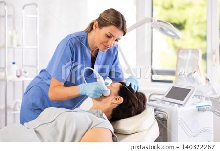 Cosmetologist performing anti-aging face hardware therapy procedure for aged female client in clinic of aesthetic medicine Cosmetologist performing anti-aging face hardware therapy procedure for aged female client in clinic of aesthetic medicine 140322267
