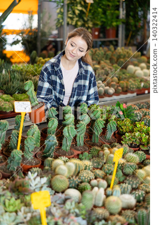 Girl works as auxiliary worker in plant store warehouse, review cactus seedling Girl works as auxiliary worker in plant store warehouse, review cactus seedling 140322414
