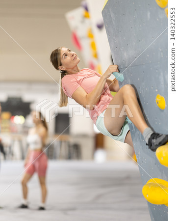 Woman climbs artificial wall bouldering, working out in gym Woman climbs artificial wall bouldering, working out in gym 140322553