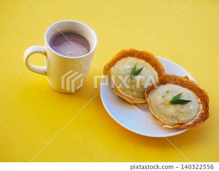 Traditional Indonesian sweet snack Serabi or coconut milk pancakes garnished with a piece of pandan leaf, served on a white plate against a vibrant yellow background with copy space. 140322556