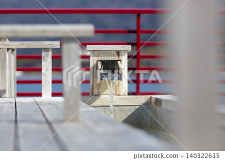 A close-up of the hot spring water flowing from the footbath spout and the red handrail. A close-up of the hot spring water flowing from the footbath spout and the red handrail. 140322615