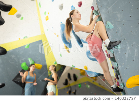 Sportive girl climbing on artificial rock wall in rock climbing gym Sportive girl climbing on artificial rock wall in rock climbing gym 140322757