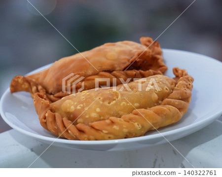 Close-up of traditional Indonesian savory snack Pastel, a crispy deep-fried pastry filled with vegetables and meat, served on a white plate. Close-up of traditional Indonesian savory snack Pastel, a crispy deep-fried pastry filled with vegetables and meat, served on a white plate. 140322761
