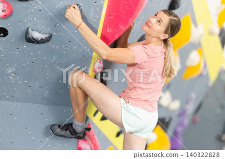 Woman climbs artificial wall bouldering, working out in gym 140322828