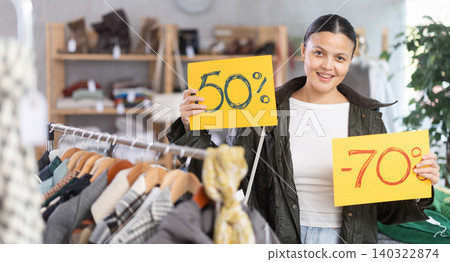 Happy asian young woman holding sign saying Sale for autumn-winter season standing in interior of clothing boutique Happy asian young woman holding sign saying Sale for autumn-winter season standing in interior of clothing boutique 140322874