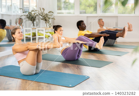 Girl performing half boat pose during group yoga session Girl performing half boat pose during group yoga session 140323282