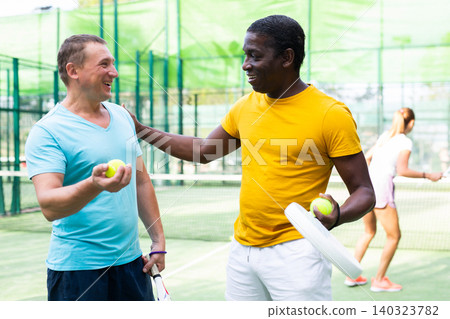 Two men padel tennis players on an outdoor court discussing something Two men padel tennis players on an outdoor court discussing something 140323782