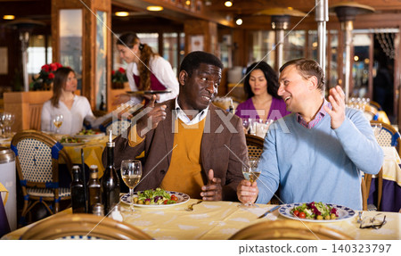 Two male friends drinking wine and chatting in restaurant 140323797
