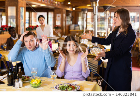 Resentful wife scolding her husband spending time with another woman at dinner 140323841
