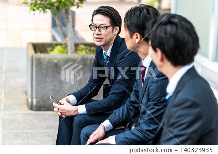Three Japanese businessmen in suits chatting outdoors. Three Japanese businessmen in suits chatting outdoors. 140323935