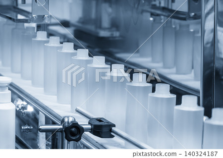 Row of liquid cosmetics bottles moving along a conveyor belt in an automated production line. Row of liquid cosmetics bottles moving along a conveyor belt in an automated production line. 140324187