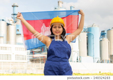 Positive girl in overalls with the Cambodia flag in her hands against the background of chimneys of modern factory Positive girl in overalls with the Cambodia flag in her hands against the background of chimneys of modern factory 140324283