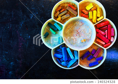 Closeup of vibrant a rainbow color range pastel chalks arranged in a flower shaped palette on a textured dark surface. Art, creativity, design concepts. Top view 140324328