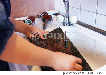 Hands of art school student cleaning a carved woodblock under a stream of running water in a white sink in printmaking studio Hands of art school student cleaning a carved woodblock under a stream of running water in a white sink in printmaking studio 140324353