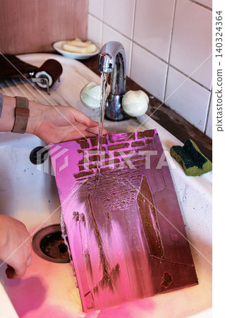 A person is rinsing a printmaking plate covered in purple ink under running water in a white sink. Movement effect A person is rinsing a printmaking plate covered in purple ink under running water in a white sink. Movement effect 140324364