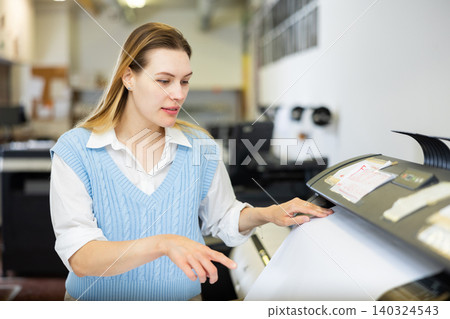 Woman employee of printing house puts a sheet of paper into plotter Woman employee of printing house puts a sheet of paper into plotter 140324543
