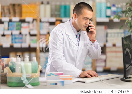 Male pharmacist working at computer and talking on phone Male pharmacist working at computer and talking on phone 140324589