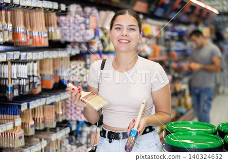 Smiling young woman choosing brushes in local hardware store Smiling young woman choosing brushes in local hardware store 140324652