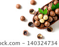 Top View of Macadamia Nuts in Wicker Basket with Cracked Shells and Green Leaves on White Background 140324734
