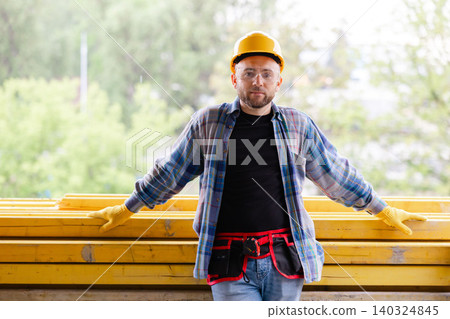 Construction worker wearing helmet and safety glasses, hands resting on timber Construction worker wearing helmet and safety glasses, hands resting on timber 140324845