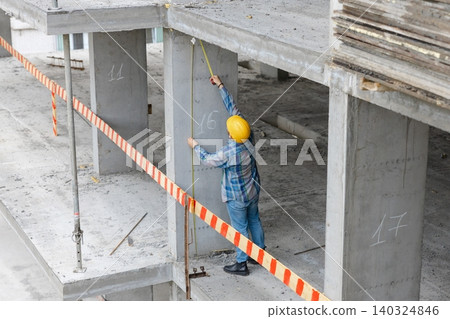 Construction worker measuring concrete column at building site Construction worker measuring concrete column at building site 140324846