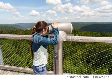 Girl looking through binoculars at scenic viewpoint on sunny day 140325153