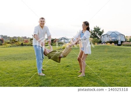 Parents Spending Time Playing With Their Son on a Green Lawn in the Backyard Under the Warm, Sunny Sky Parents Spending Time Playing With Their Son on a Green Lawn in the Backyard Under the Warm, Sunny Sky 140325318