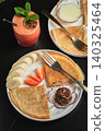 A plate of crepes filled with chocolate spread and topped with banana slices and mint 140325464
