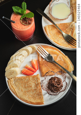 A plate of crepes filled with chocolate spread and topped with banana slices and mint 140325464