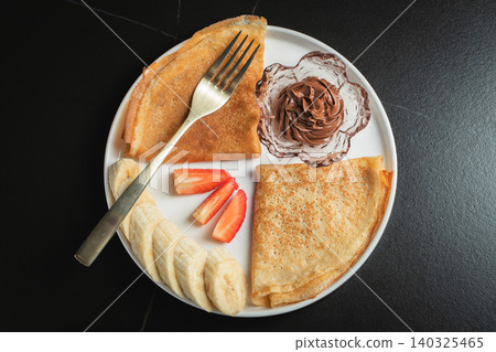 A plate of crepes filled with chocolate spread and topped with banana slices and mint 140325465