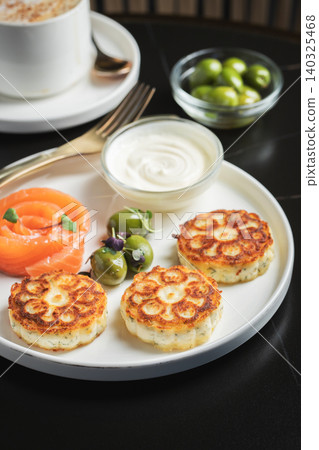 Savory Syrniki with Smoked Salmon, Olives and Sour Cream on White Plate Savory Syrniki with Smoked Salmon, Olives and Sour Cream on White Plate 140325468