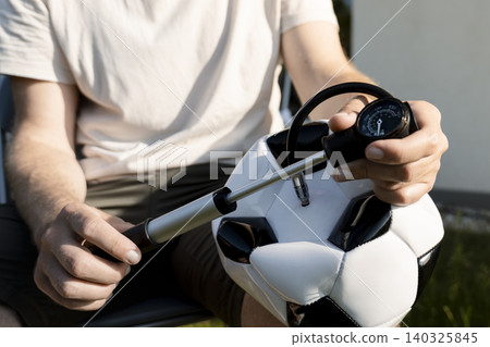 Person inflating a classic black and white soccer ball with a hand pump, showing everyday actions connecting to global sport. 140325845