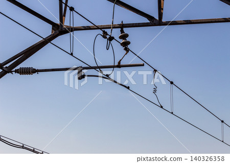 A close-up of railway overhead wires and support devices (movable brackets) against a clear blue sky. A close-up of railway overhead wires and support devices (movable brackets) against a clear blue sky. 140326358