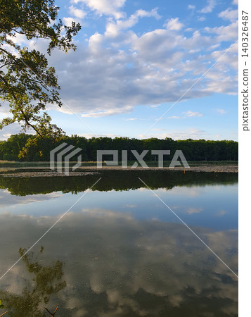 Picturesque summer landscape: mirror lake with reeds, reflection of clouds in the water, green forest on the horizon Picturesque summer landscape: mirror lake with reeds, reflection of clouds in the water, green forest on the horizon 140326487