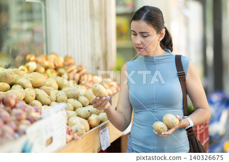 Middle-aged woman choosing potato in big supermarket 140326675