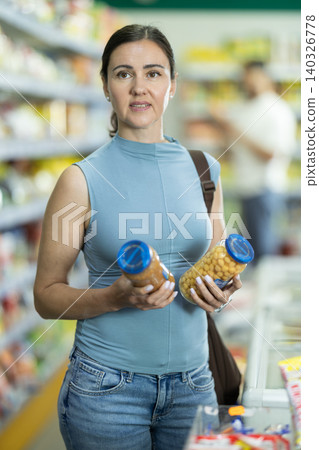 Middle-aged woman choosing canned goods in supermarket Middle-aged woman choosing canned goods in supermarket 140326778
