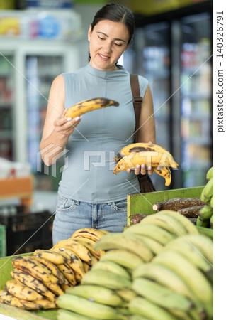 Middle-aged woman choosing plantain bananas in supermarket Middle-aged woman choosing plantain bananas in supermarket 140326791
