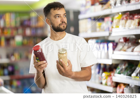 Middle-aged man choosing canned goods in supermarket Middle-aged man choosing canned goods in supermarket 140326825