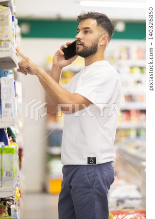Man talks on phone and chooses baby formula and consults with his wife. Man talks on phone and chooses baby formula and consults with his wife. 140326850