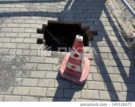 Traffic cone and hole on brick paved sidewalk, illustrating urban maintenance concept Traffic cone and hole on brick paved sidewalk, illustrating urban maintenance concept 140326875