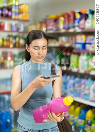 Before making purchase, woman buyer scans barcode code on packaging of fabric liquid detergent follows link and reads information about product on manufacturers website Before making purchase, woman buyer scans barcode code on packaging of fabric liquid detergent follows link and reads information about product on manufacturers website 140326897