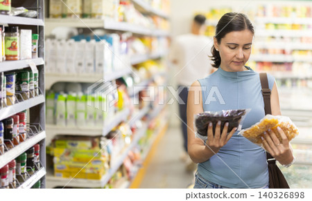 Female shopper carefully selects noodles at grocery supermarket Female shopper carefully selects noodles at grocery supermarket 140326898